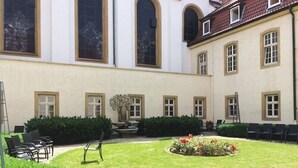 Un patio con una fuente, zona de estar y un edificio con ventanas amplias y techo de tejas.