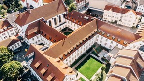 Vista aérea de un complejo histórico de edificios interconectados, con un patio central y diferentes estilos de tejados.