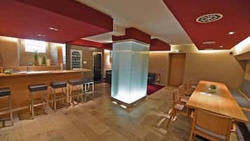 Un moderno vestíbulo de hotel con zona de bar, asientos y un elemento decorativo luminoso central.