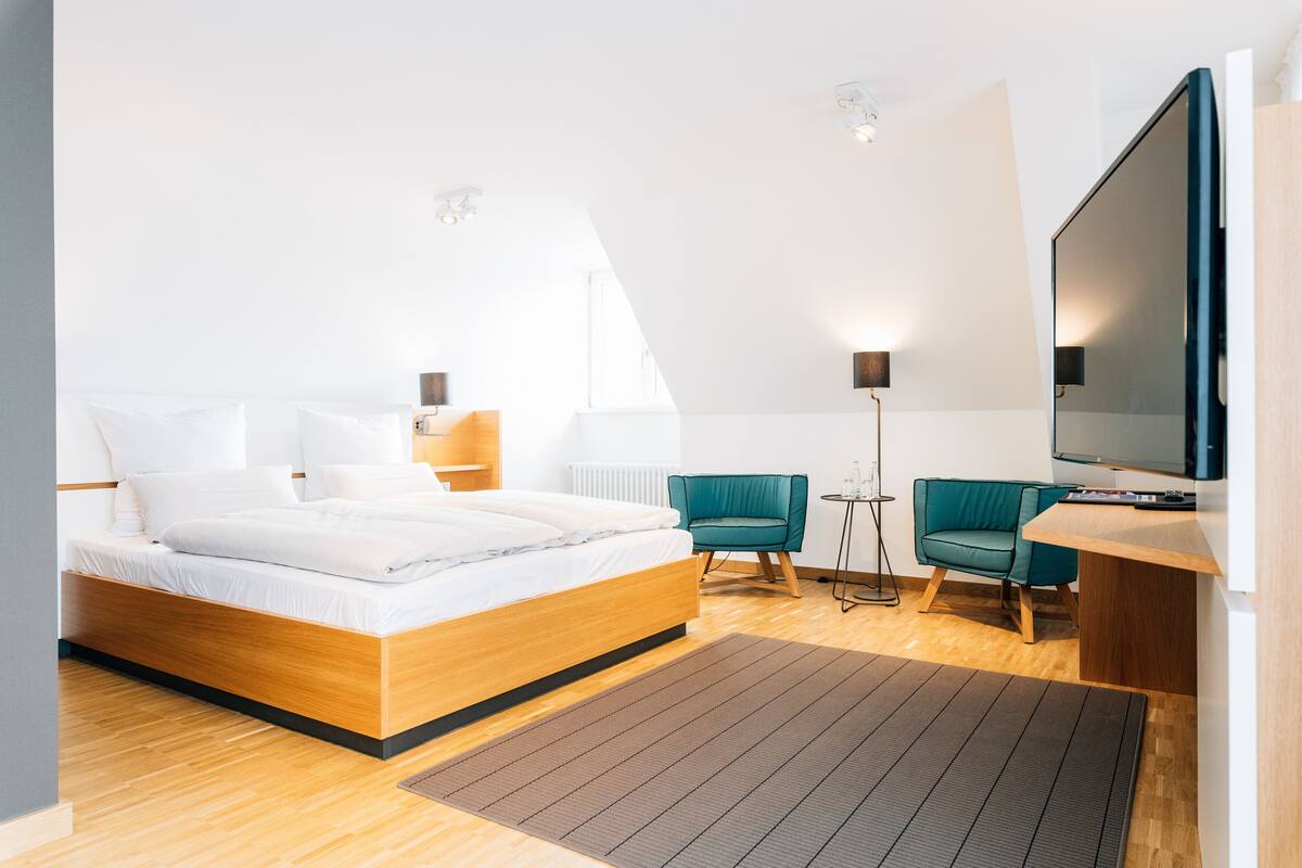 A modern hotel room with a wooden bed, a desk, a TV, and two chairs.
