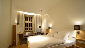 Habitación de hotel con una cama grande, mesitas de noche, un escritorio, una silla y una ventana con cortinas.