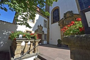 A courtyard with a stone staircase leading to a building entrance, surrounded by flowering plants and a large stone planter. - Bildungs- und Tagungshaus Liborianum (Paderborn)