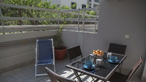 Ett bord med glasskiva och fyra stolar, en krukväxt och en skål med apelsiner.