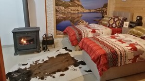 Un dormitorio acogedor con una estufa de leña, una cama grande con ropa de cama estampada y un mural pintado con un paisaje.