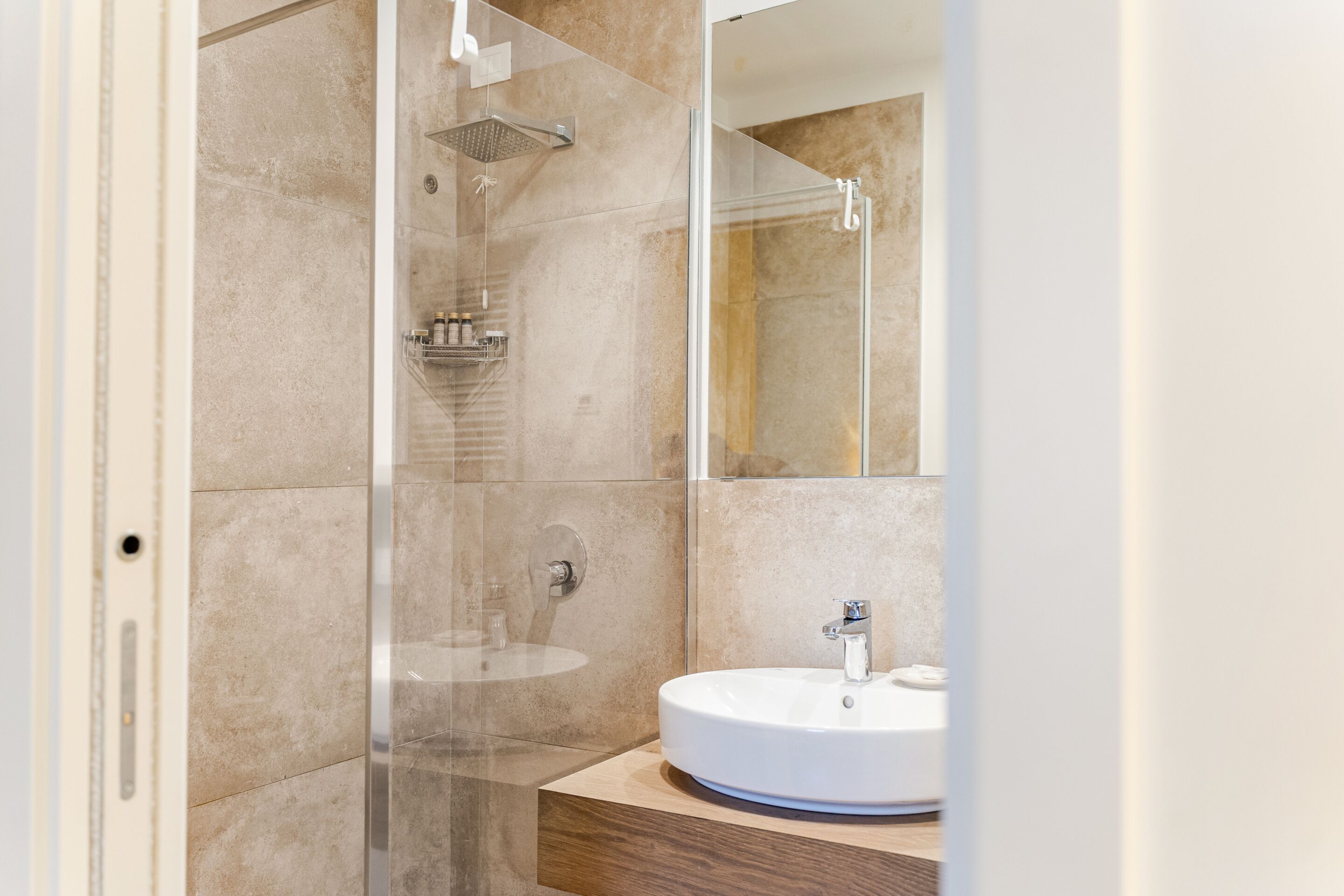 Un baño moderno con ducha envuelta en vidrio, un lavabo redondo y un mueble de tocador de madera.