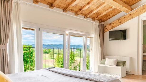 Un dormitorio con una cama grande, televisión y balcón con vistas a zonas verdes y montañas.