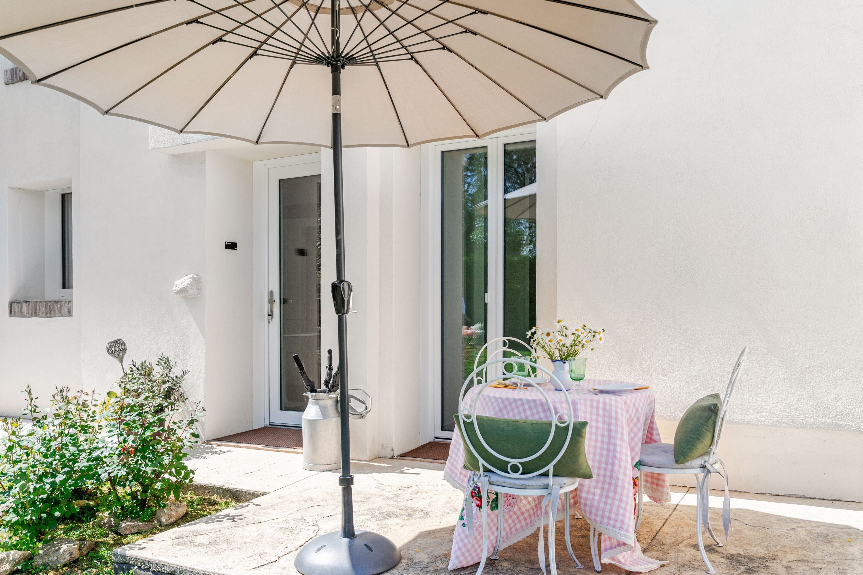 Eine Terrasse im Freien mit einem für zwei Personen gedeckten Tisch, einem Stuhl, einem Sonnenschirm und einem kleinen Gartenbereich.