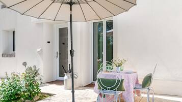 Eine Terrasse im Freien mit einem für zwei Personen gedeckten Tisch, einem Stuhl, einem Sonnenschirm und einem kleinen Gartenbereich.
