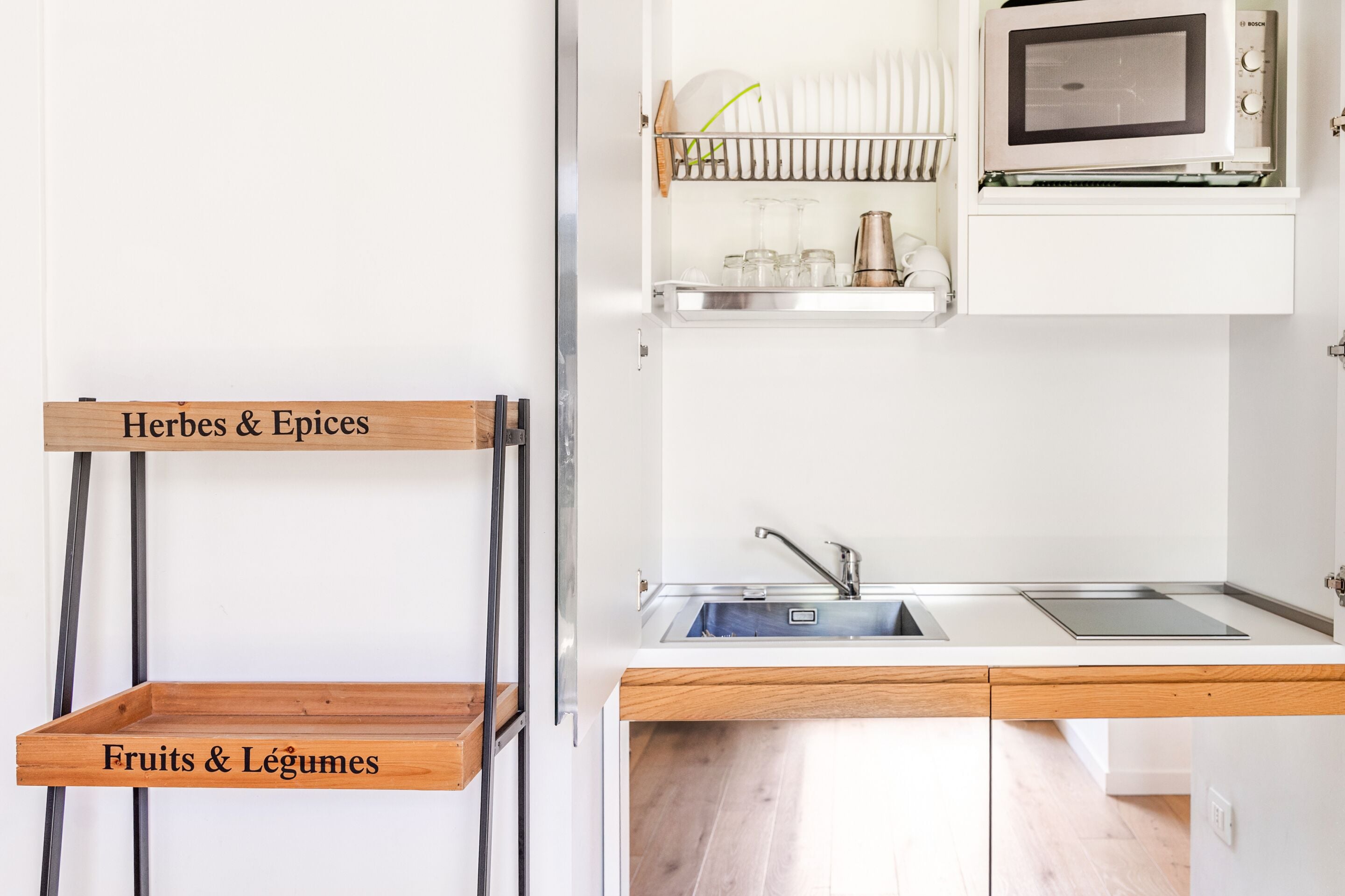A kitchen with a microwave, sink, and wooden shelves labeled 'Herbes & Epices' and 'Fruits & Légumes'.
