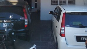 A two-story building with a sign for "H.J. Ismail Homestay 2" and contact numbers. There are two parked cars, one black and one white, in front of the building. - Homestay Haji Ismail 5 bedrooms 2 Aircond (Kota Bharu)