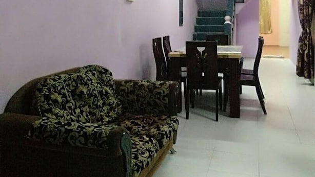 A living room with a sofa, dining table, chairs, and a staircase leading to another room. - Homestay Haji Ismail 5 bedrooms 2 Aircond (Kota Bharu)