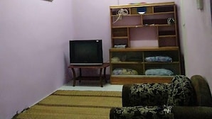 A living room with a television, a sofa, a wooden shelf unit, and a painting on the wall. - Homestay Haji Ismail 5 bedrooms 2 Aircond (Kota Bharu)