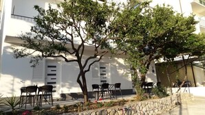 A building with a white facade, outdoor seating area, and a stone wall. - Apartment in Podgora with Terrace, Air condition, WIFI (4492-6) (Podgora)