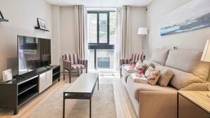 Een moderne woonkamer met een flatscreen televisie, een bank, een salontafel en gestreepe fauteuils.