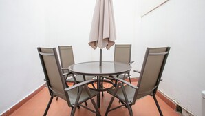 Ein runder Tisch mit vier Stühlen und Sonnenschirm in einem Raum mit weißen Wänden und Fliesenboden.