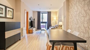 Ein modernes Hotelzimmer mit Essbereich, Sofa, Fernseher und Blick auf die Stadt.