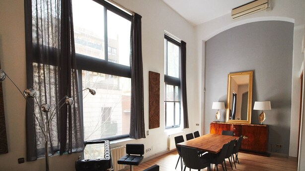A dining area with a wooden table, black chairs, a mirror, and a radiator. - Alcam Alio Cine (Barcelona)
