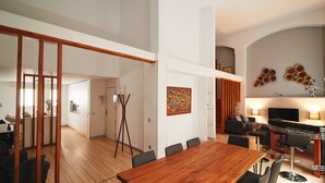A spacious living area with a wooden dining table, black chairs, a modern sofa, and a TV. - Alcam Alio Cine (Barcelona)