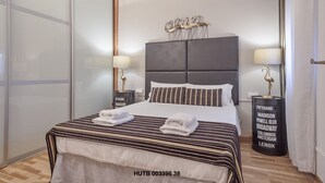 Moderni hotellihuone, jossa on suuri sänky, raidallinen vuodevaatteisto ja kaksi yöpöytää, joissa on lamput.