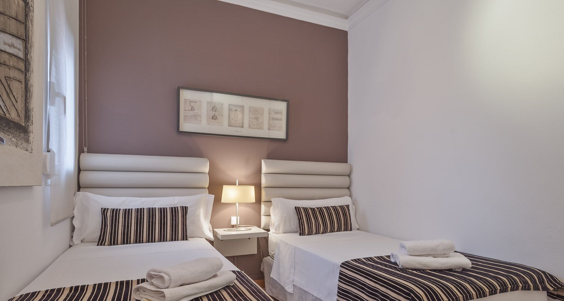 Una camera d'albergo con due letti, un comodino, una lampada e un quadro appeso al muro.