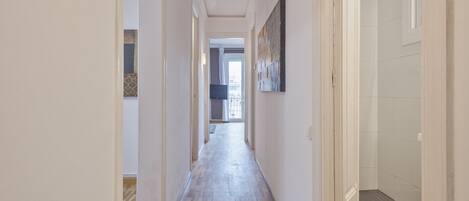 A hallway with a wooden floor, white walls, and a door on the right.