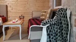 Et hyggeligt rum med træloft, en seng med et rød- og sortternet tæppe, et lille bord med stearinlys og et vindue med udsigt.