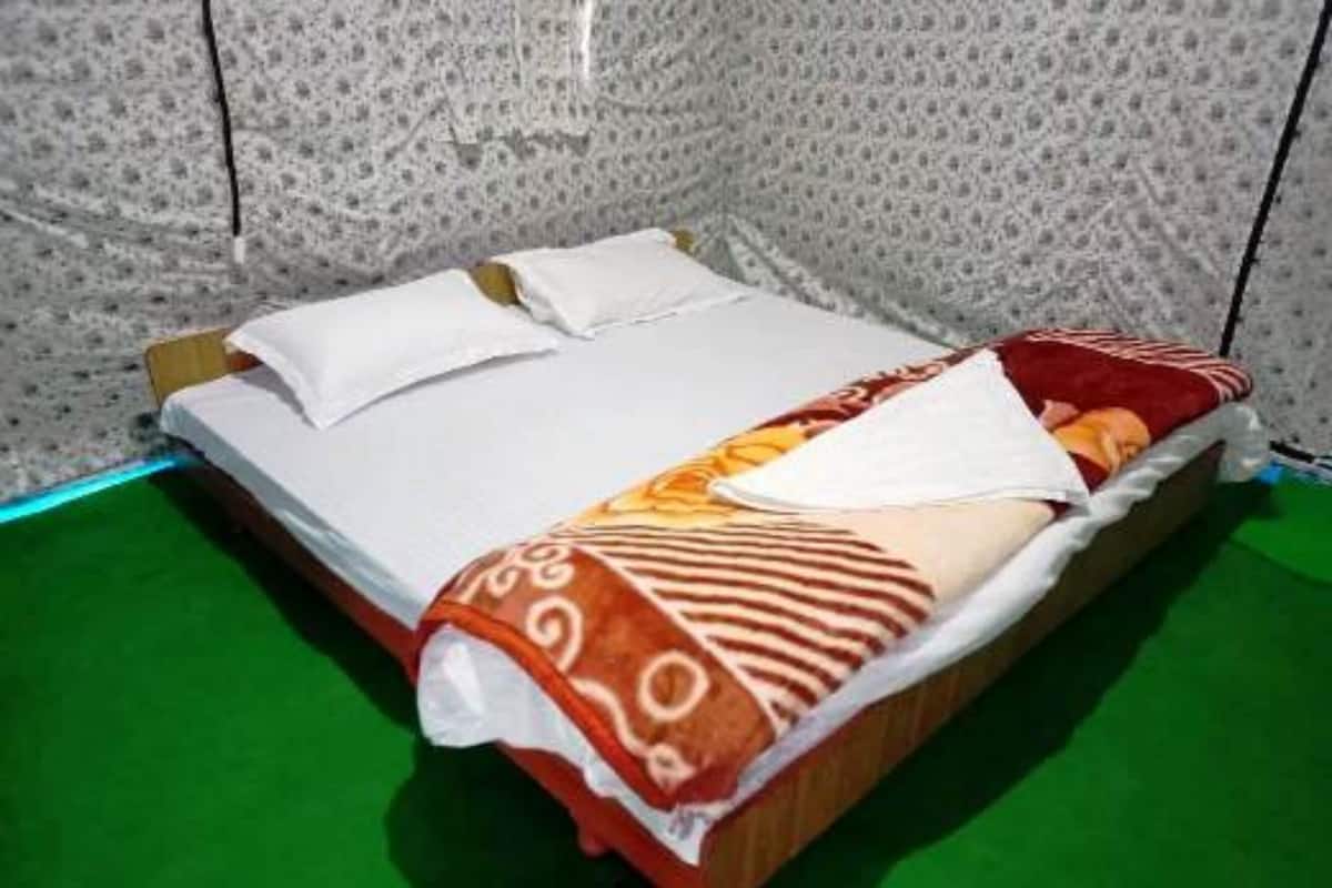 Een bed met een gebloemd plaid, witte kussens en een groene vloer.
