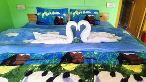 Un lit recouvert d’une couvre-lit bleue ornée d’un motif représentant un paysage, deux oreillers assortis et une tête de lit en bois.