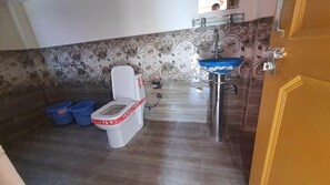 A bathroom with a toilet, sink, and two blue buckets on the floor.