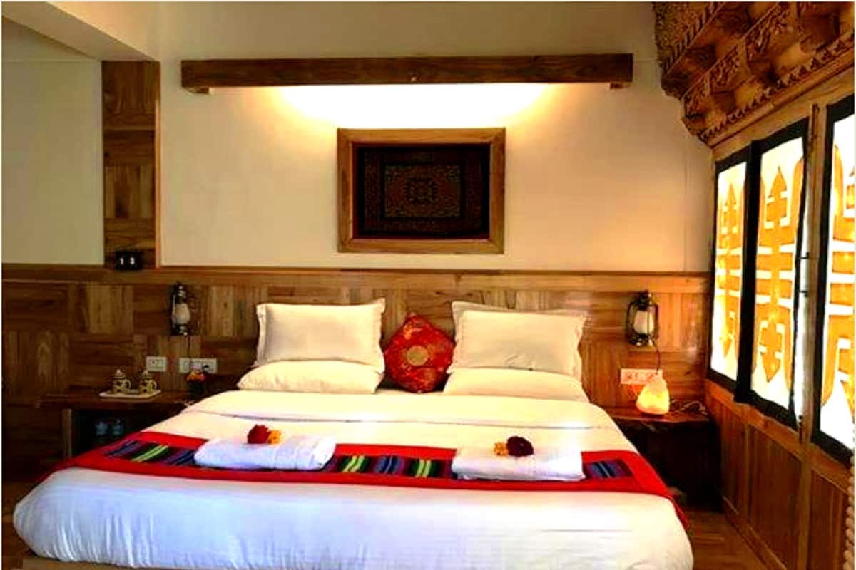 A hotel room with a wooden headboard, a large bed with white linens, a red and white striped blanket, and a decorative wall hanging.