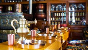 A room with a long wooden table displaying various metal containers and a traditional brass tea set. - TIH Namra Village Hotel - Temisgam (Leh)