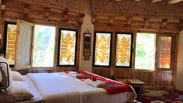 A wooden room with a bed, windows with decorative frames, and a red carpet. - TIH Namra Village Hotel - Temisgam (Leh)
