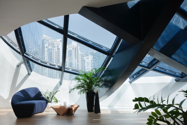 Ein modernes Interieur mit gewölbter Decke, einem großen Fenster mit Stadtblick, einem blauen Sessel und einem Blumentopf.