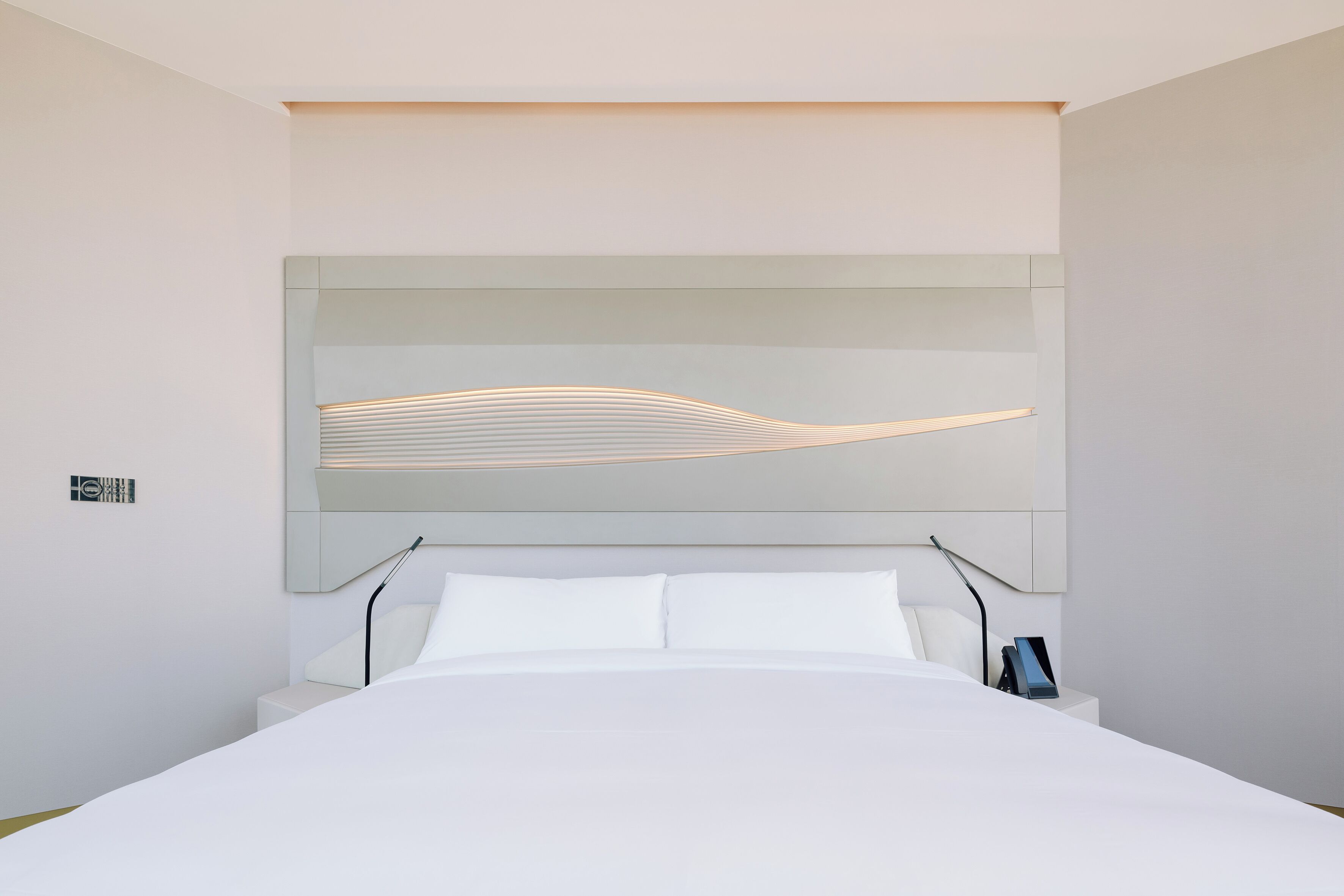 Une chambre d’hôtel moderne dotée d’un grand lit, d’une tête de lit avec éclairage intégré et d’une table de chevet avec une lampe.
