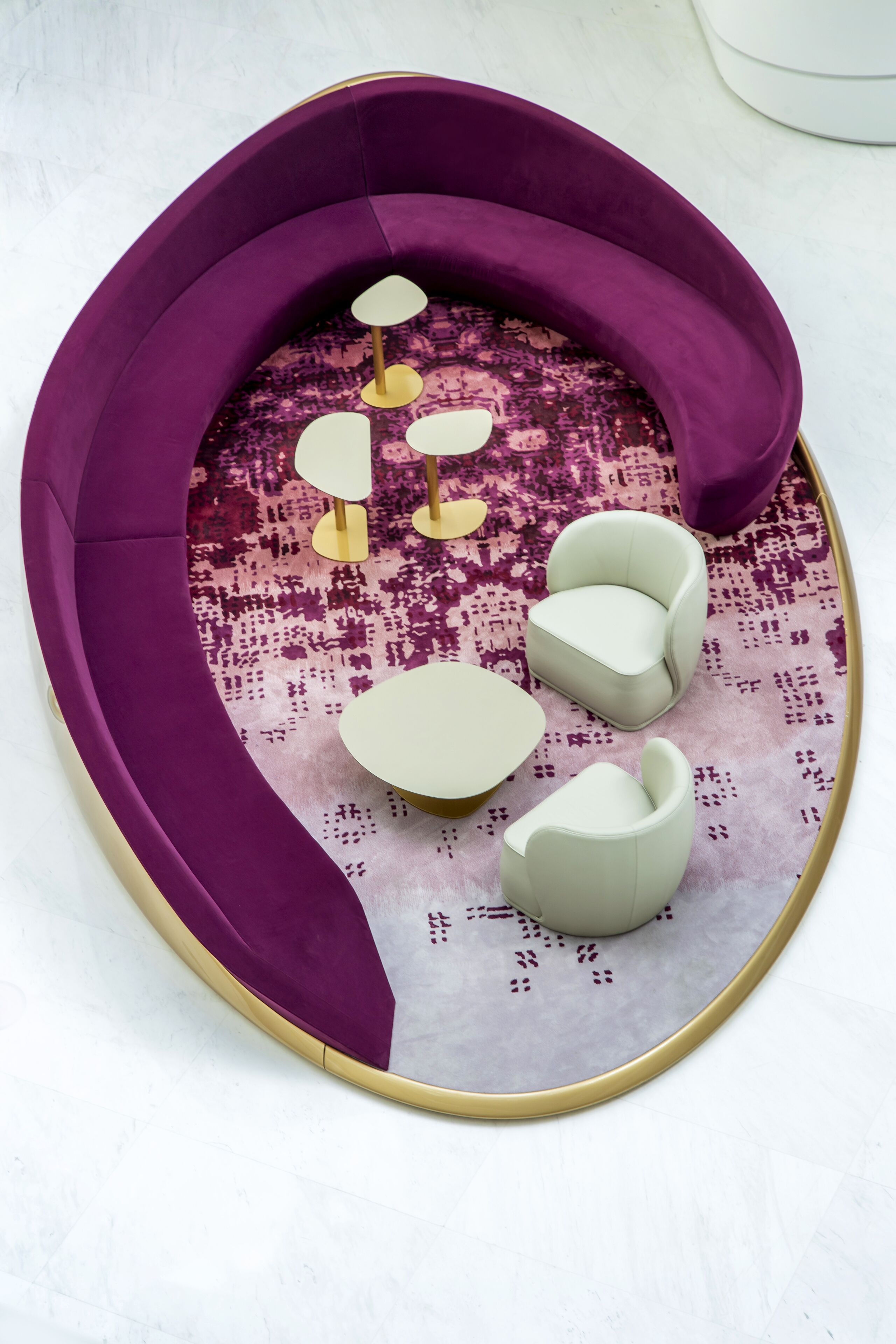 Um sofá roxo com um tapete estampado, uma mesinha e um candeeiro dourado.