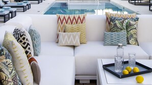Un área de piscina en la azotea con un sofá blanco, sillones reclinables y una mesa de billar.