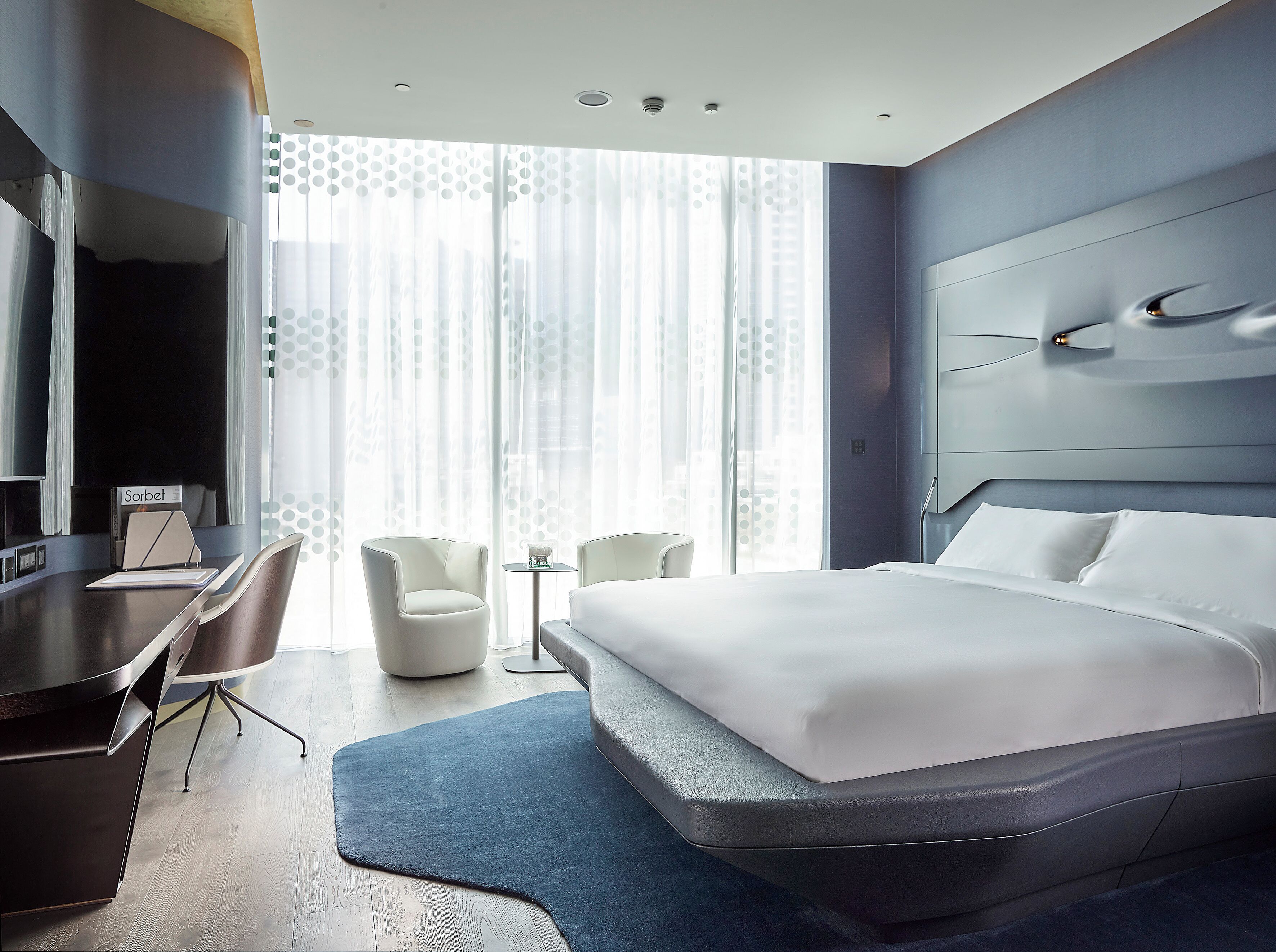 Ein modernes Hotelzimmer mit einem großen Bett, einem Schreibtisch, zwei Stühlen und einem Fernseher.