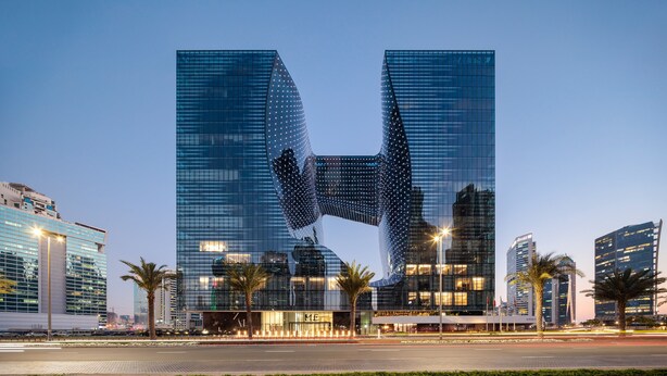 Un edificio moderno con un diseño arquitectónico único, que presenta un amplio frente de vidrio reflectante y una estructura curva distintiva en el centro.
