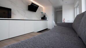 A modern kitchen with a built-in TV, white cabinetry, and a grey sofa in the living area. - State-of-the-art studio with frontal sea view (Koksijde-Bad)