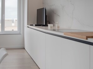 Une cuisine moderne dotée d’une grande fenêtre donnant sur une plage, d’un téléviseur à écran plat et d’une planche à découper en bois posée sur le plan de travail.