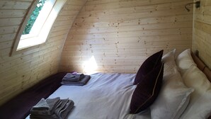 A cozy, single-room cabin with a sloped ceiling, a small window, and a neatly made bed with pillows and folded towels.