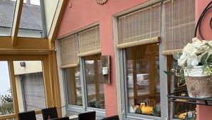 A restaurant with outdoor seating, featuring wooden tables and black chairs, with a red wall and a decorative sun motif above the windows. - Hotel Seebach (Grossenseebach)