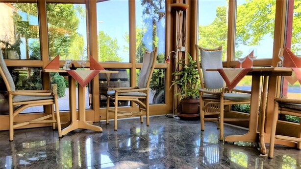 A room with large windows, a polished marble floor, and several wooden chairs with unique back designs. - Hotel Seebach (Grossenseebach)