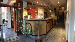 A hotel reception area with a counter, potted plants, and a staircase in the background. - Hotel Seebach (Grossenseebach)