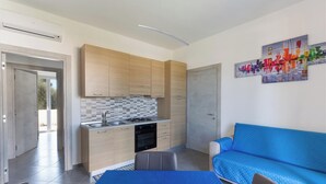 Een moderne keuken met houten kastjes, een betegelde achterwand en een blauwe bank in de woonkamer.