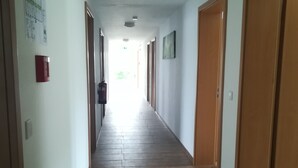 A long, narrow hallway with wooden flooring and white walls. There are doors on both sides, and a fire alarm is mounted on the wall. - Jura Hotel (Nuremberg)