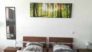 A double bed with striped bedding and green towels, a wooden headboard, a nightstand with a lamp, and a forest-themed wall art. - Jura Hotel (Nuremberg)
