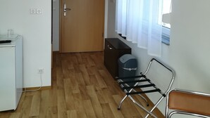 A room with a wooden floor, a desk with a chair, a radiator, a window with curtains, and a door with a sign. - Jura Hotel (Nuremberg)