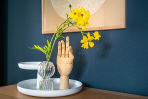 A wooden hand sculpture holding a vase with yellow flowers on a white circular table against a dark blue wall. - BodenseeApartments (Friedrichshafen)