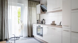 A modern kitchen with white cabinets, a built-in oven, and a window with sheer curtains. - BodenseeApartments (Friedrichshafen)